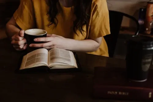 Woman holding a coffee mug while reading a book.