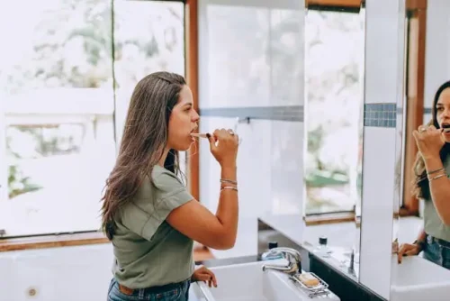 Woman brushing her teeth while looking in the mirror.