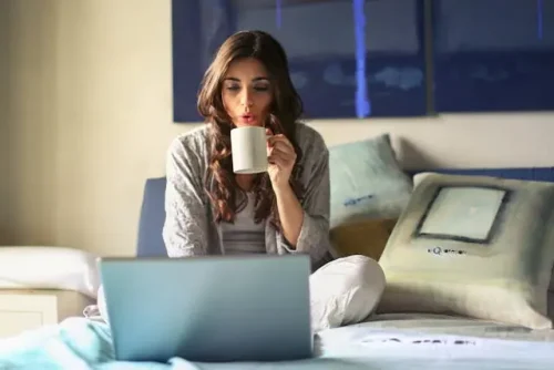 A woman sitting on the bed with a laptop and a large cup.