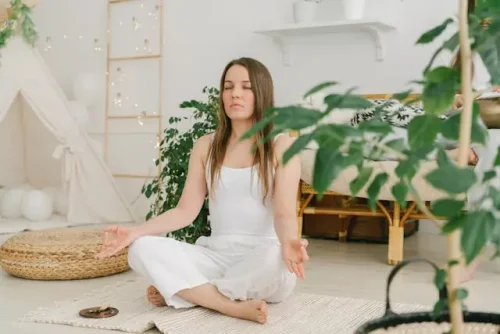 Woman meditating in a bright, minimal room surrounded by greenery, embracing calm and simplicity post-move.