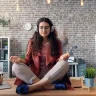 Woman practicing meditation on a desk with headphones, symbolizing healthy habits that stick in a new environment.