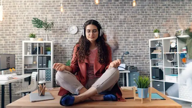 Woman practicing meditation on a desk with headphones, symbolizing healthy habits that stick in a new environment.