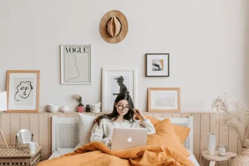 Woman sitting in bed with a laptop, creating comfort and focus in a cozy bedroom space.