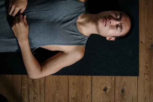 Man lying on a yoga mat with eyes closed, practicing relaxation.