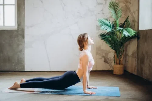 Woman in athletic wear doing upward dog on a yoga mat in a bright room with a large plant representing wellness rituals to reset